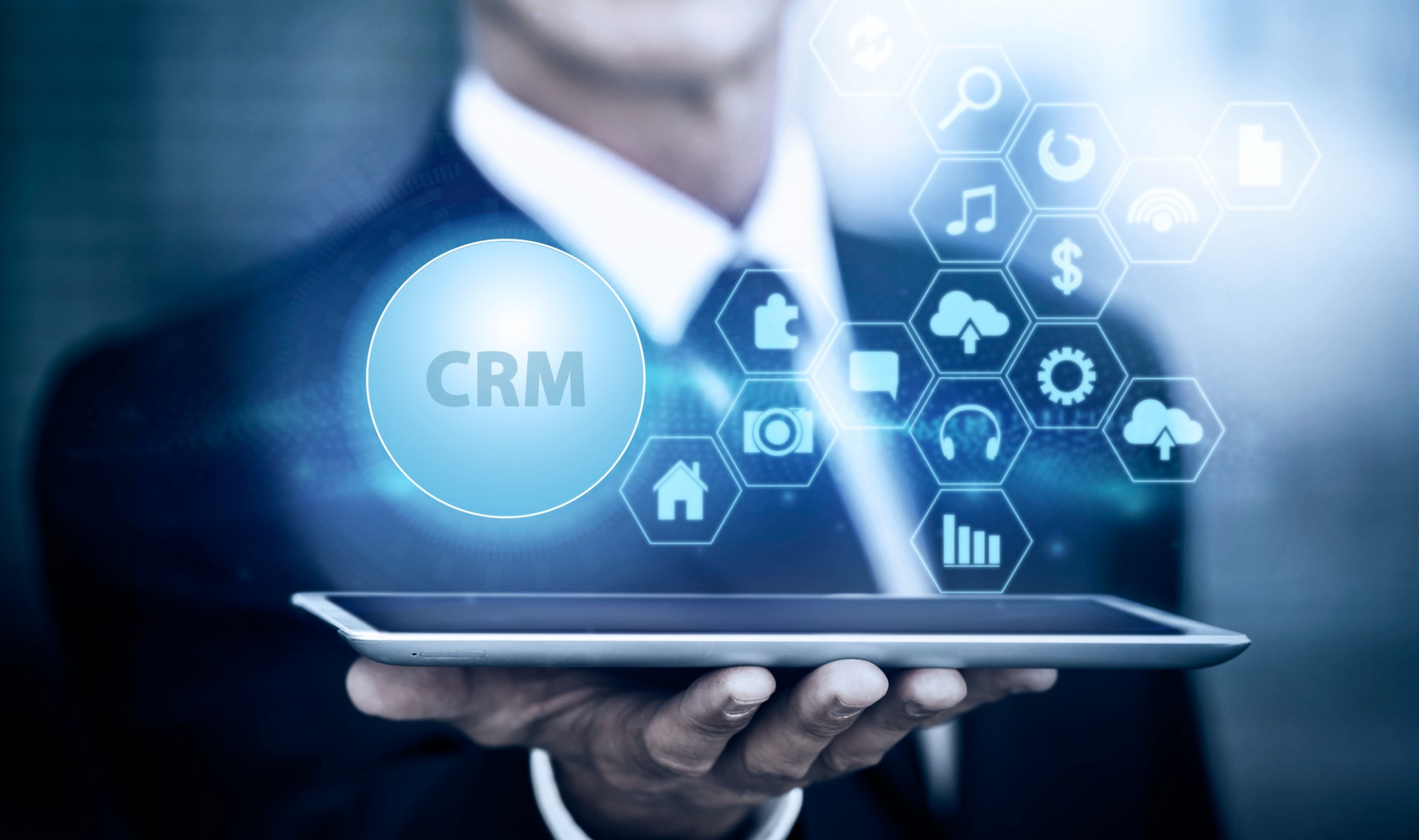 Business person holding a tablet with a floating “CRM” icon and various digital interface symbols representing technology and data management.